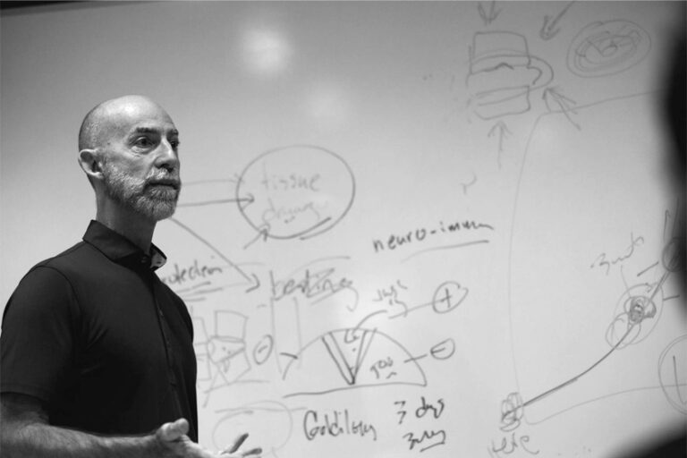 Author, Clayton Skaggs, talking with colleagues in front of a marker board